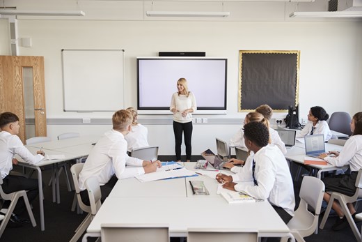 Teacher standing at front of classroom speaking to room of students